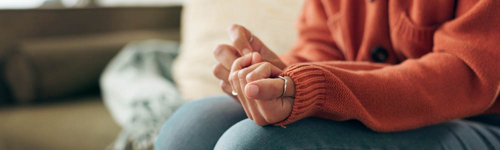 Close-up of hands and torso of a woman wringing her hands on the couch of a therapist's office
